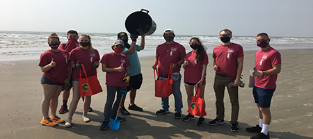 Students pose on a beach with the marine debris they collected during a beach cleanup