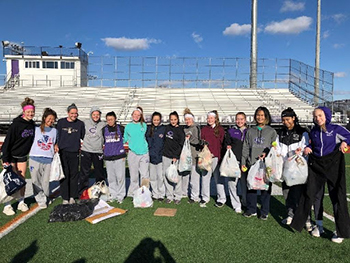 High school girls’ lacrosse team collecting recyclables from athletic field.