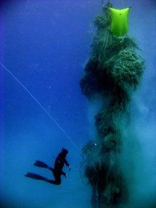 A specially trained NOAA diver confronts an enormous floating mass of marine debris, comprised mostly of derelict commercial fishing gear.
