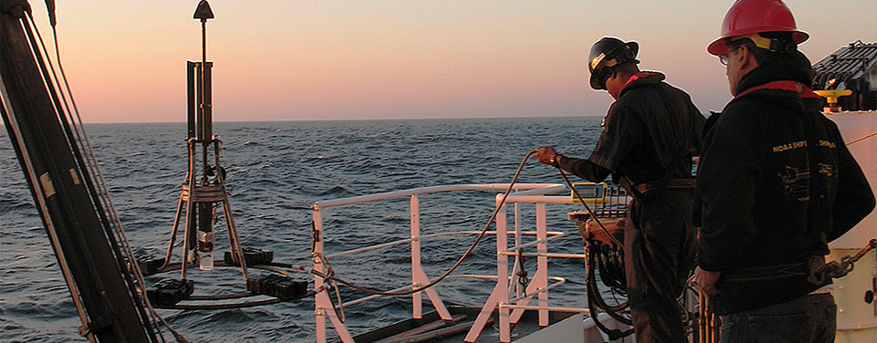 NOAA scientists guide the sediment corer back onto the deck so they can retrieve the sample.