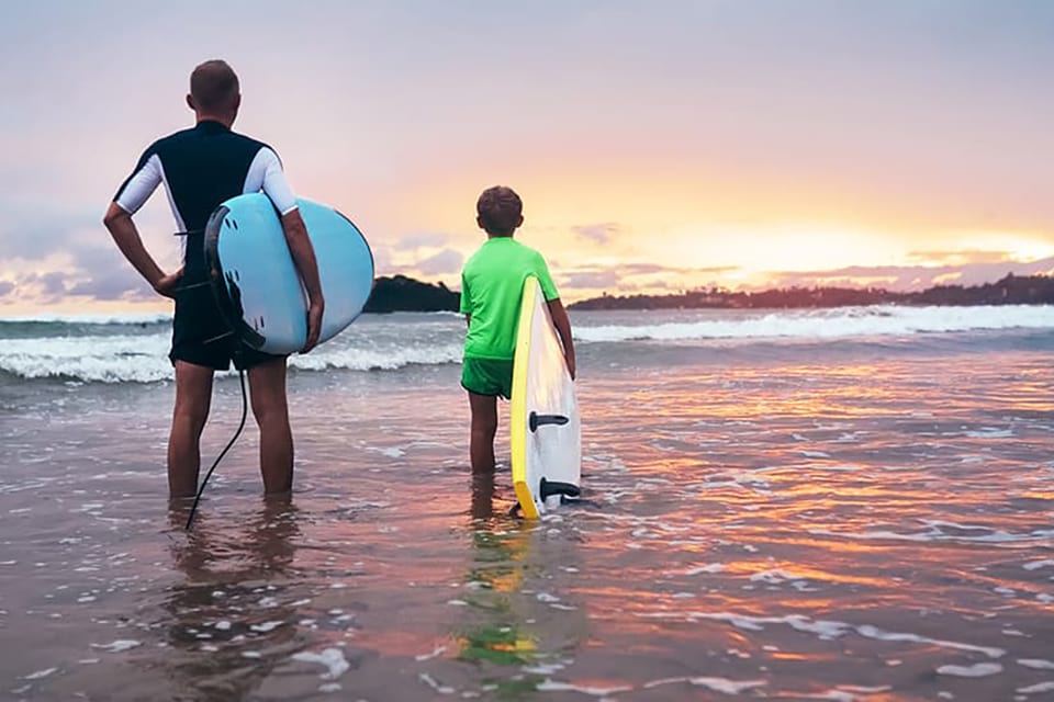 two surfers look out at the sun setting behind the oceans horizon