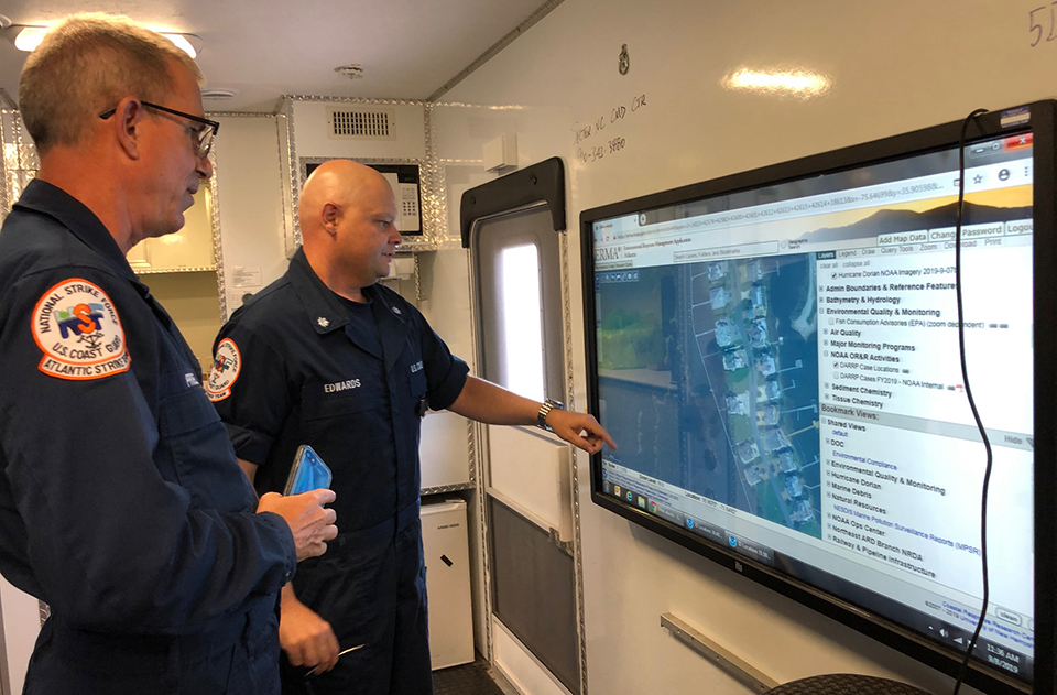 Two U.S. Coast Guard members point to a screen.