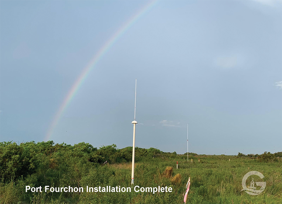 A rainbow arcs over a green field with radar instruments jutting out of the ground.