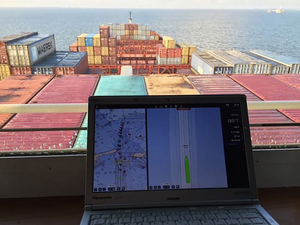 In the foreground, a laptop with navigational data. In the background, multi-colored shipping containers.