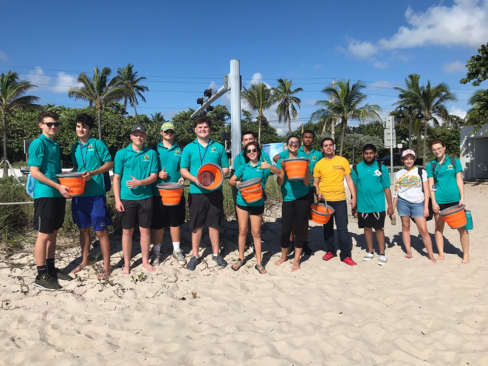 Students posing with orange buckets on the beach.