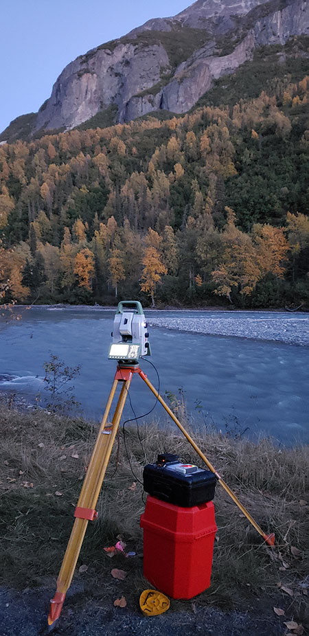 A TSACS machine sits on top of a tripod with water and trees in the background.