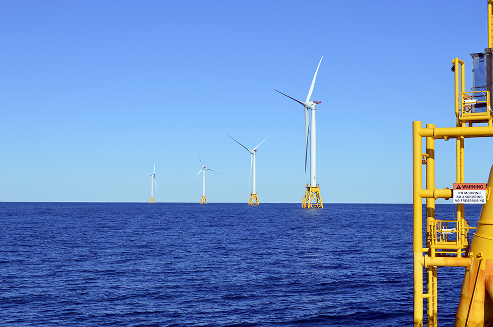 Wind farm on dark blue water with light blue sky in the background.