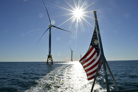 An American flag with offshore wind turbines in the background.