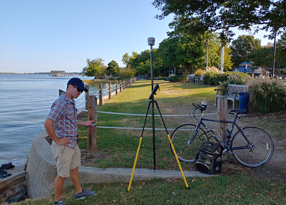 A person using survey equipment near the water.