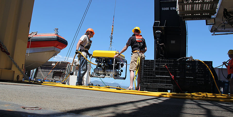 Remotely Operated Vehicle (ROV) technician Jason White (left) and oceanographer Time Battista gently maneuver the ROV over the side of the ship.