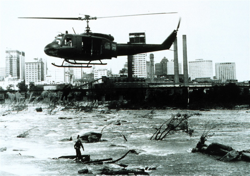 Virginia National Guard helicopter rescuing an individual from the James River. Note: rescued man halfway up to helicopter. Helicopter crewman standing on debris in river. Courtesy NWS Collection.