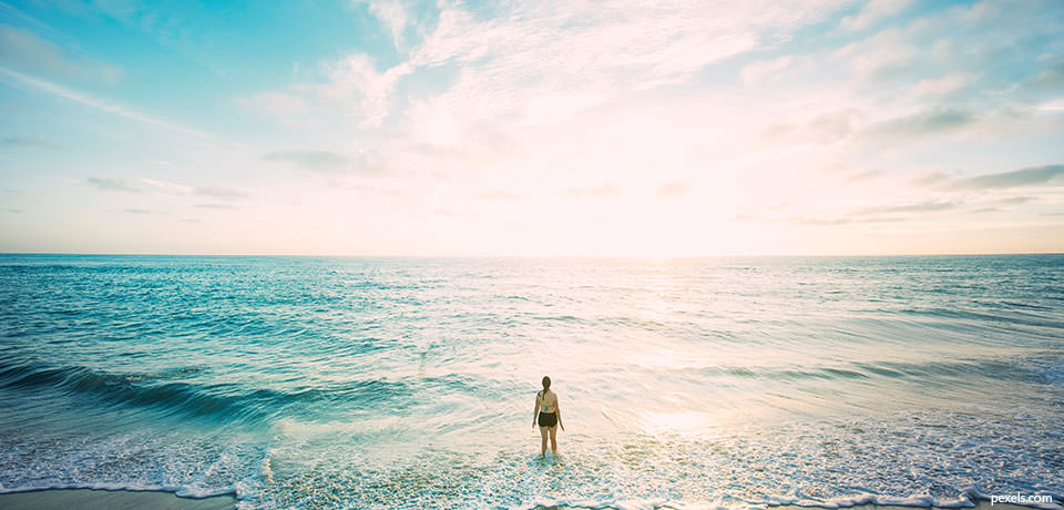 woman standing in surf looking out at ocean. Credit: pexels.com