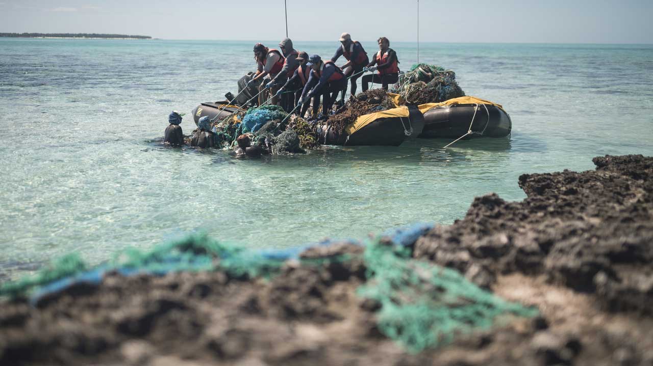A team works together to pull a large mass of nets into the boat near the barrier reef at Midway Atoll