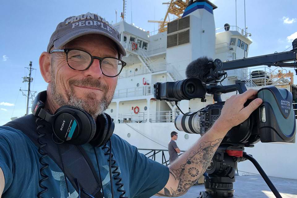 Kurt Mann holding a pro camera on the deck of the NOAA ship Ron Brown